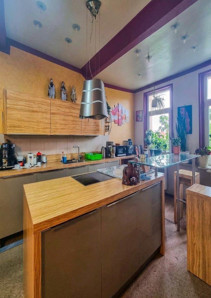 Moderne Küche mit Holzinsel, Hängelampe, Pflanzen und großen Fenstern.