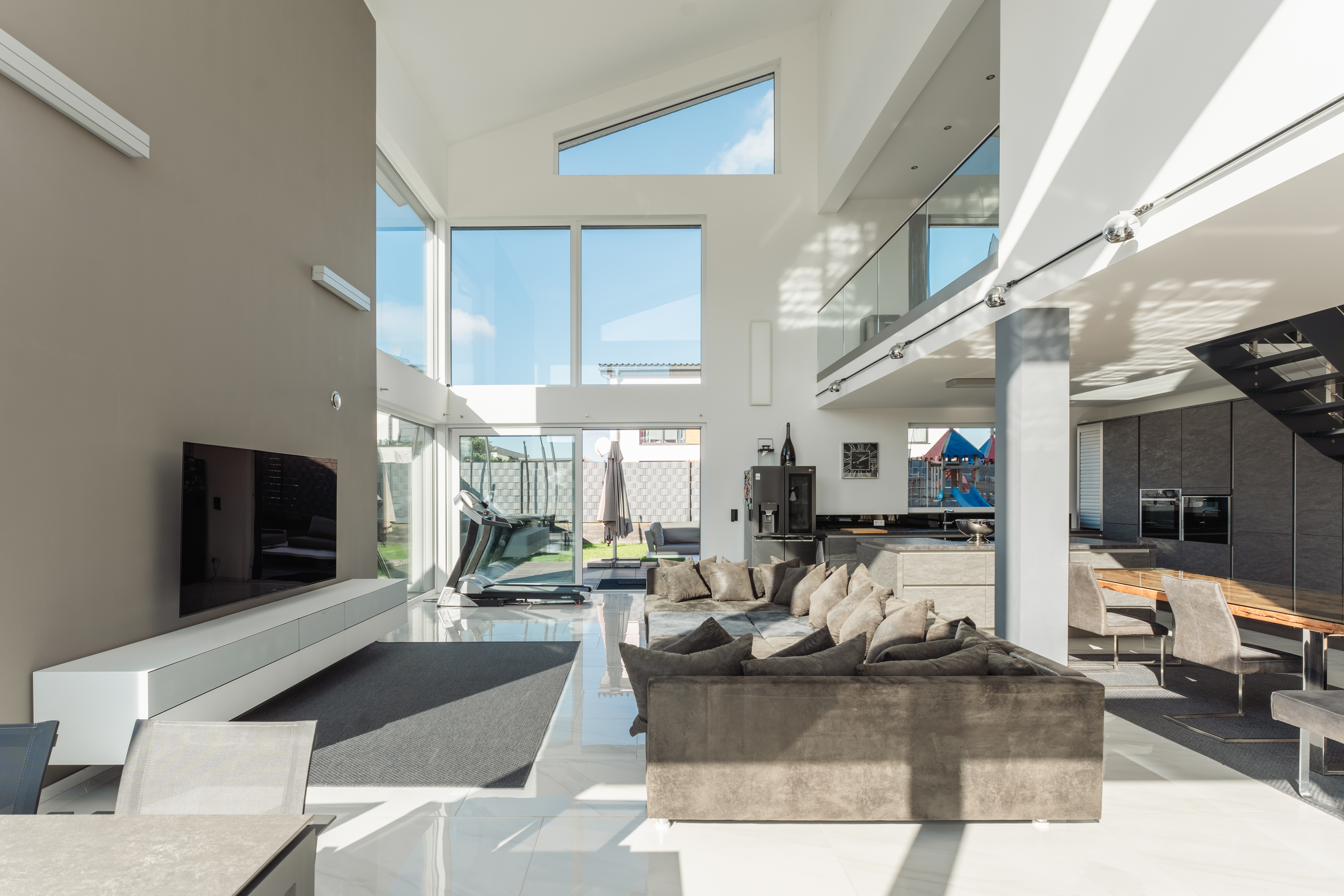Helles Wohnzimmer mit großer Fensterfront, grauem Sofa, Fernseher und moderner Einrichtung.