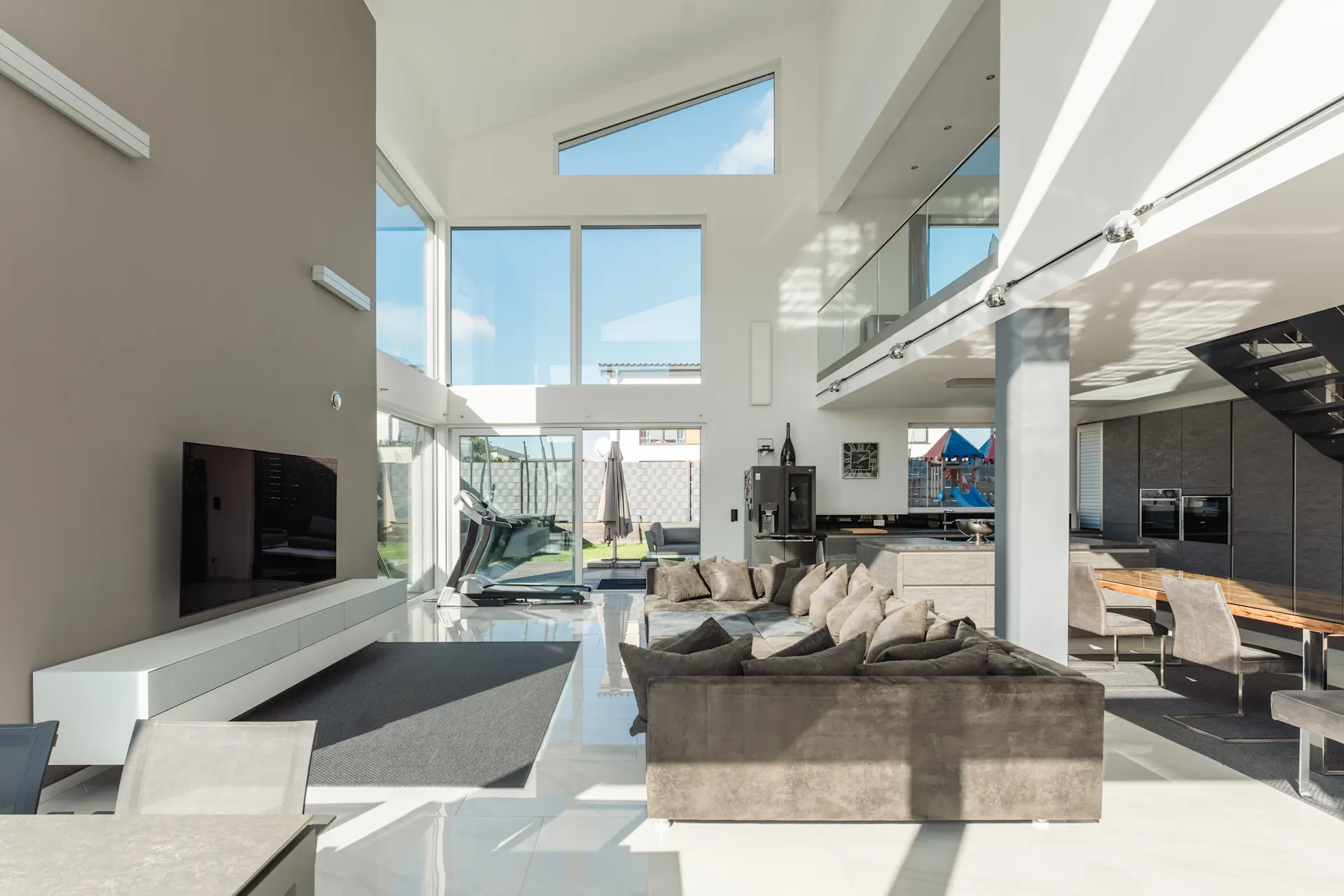 Helles Wohnzimmer mit großer Fensterfront, grauem Sofa, Fernseher und moderner Einrichtung.