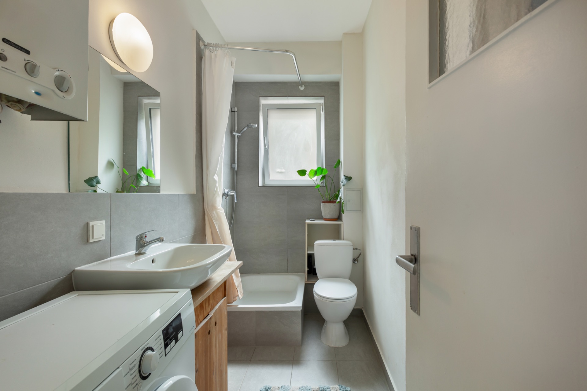Modernes Badezimmer mit Waschmaschine, Waschbecken, Dusche, Toilette und Fenster.