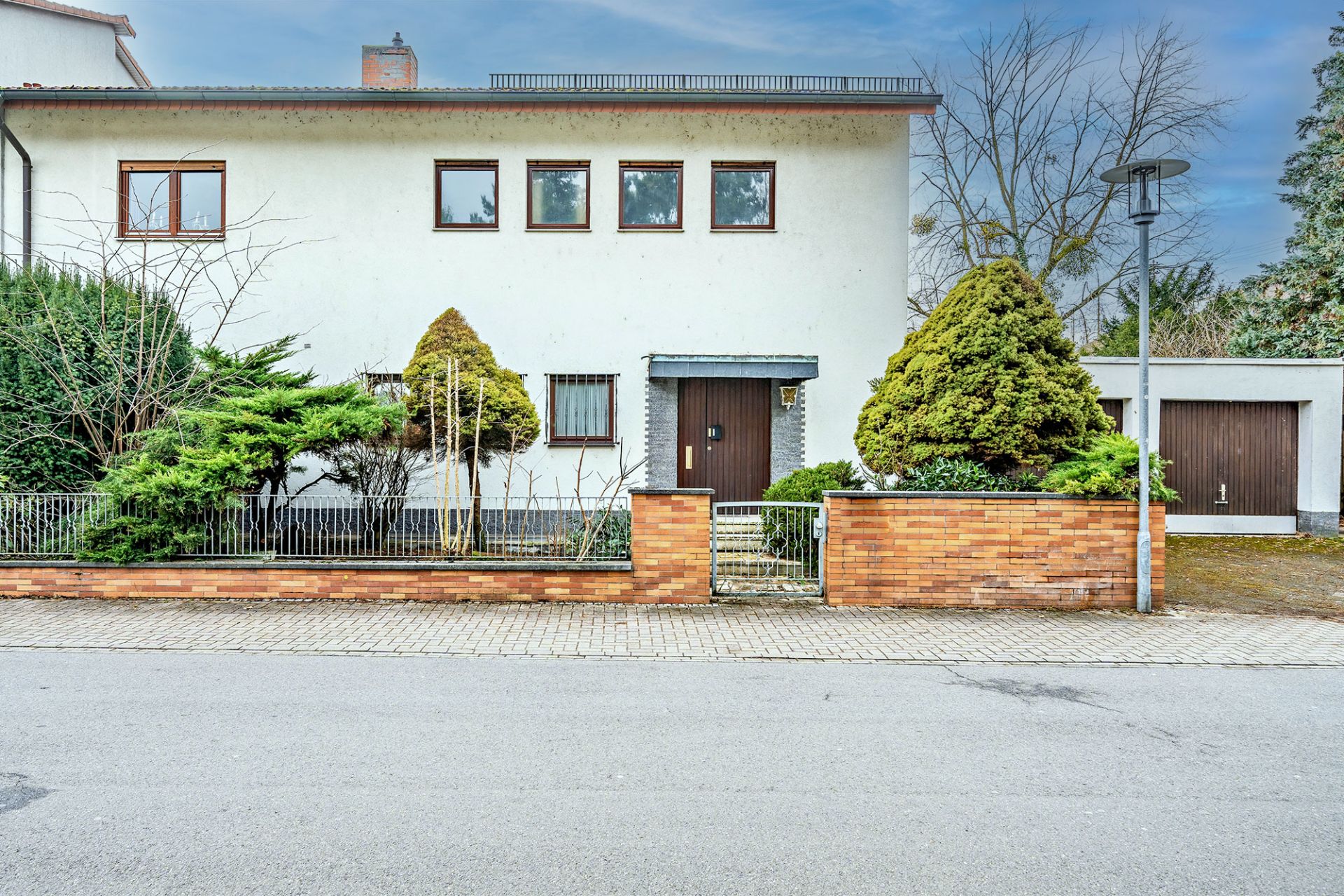 Zweistöckiges Wohnhaus mit Vorgarten, Backsteinzaun und angrenzender Garage.