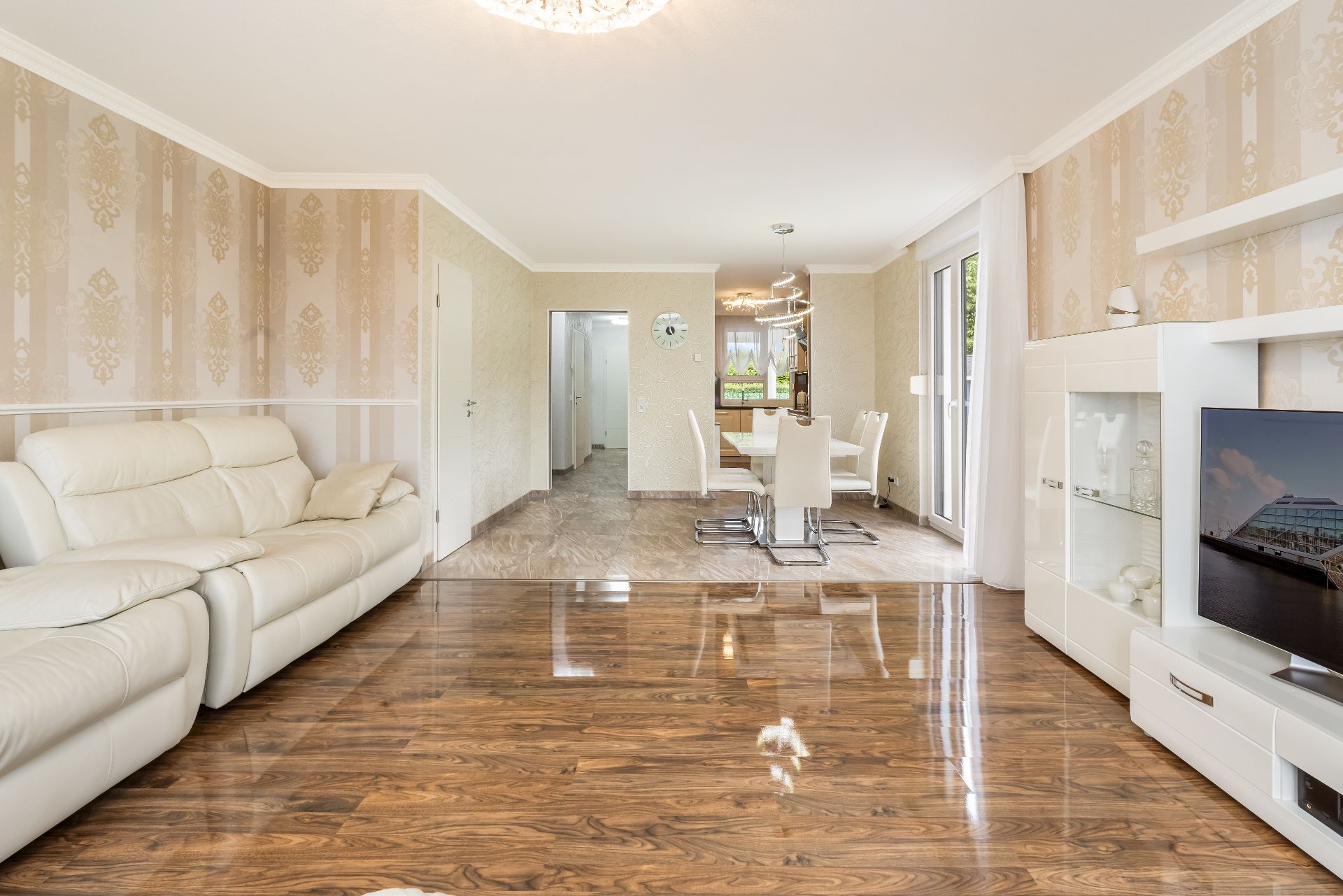 Helles Wohnzimmer mit weißem Sofa, Holzboden, Esstisch und Glastür zum Garten.