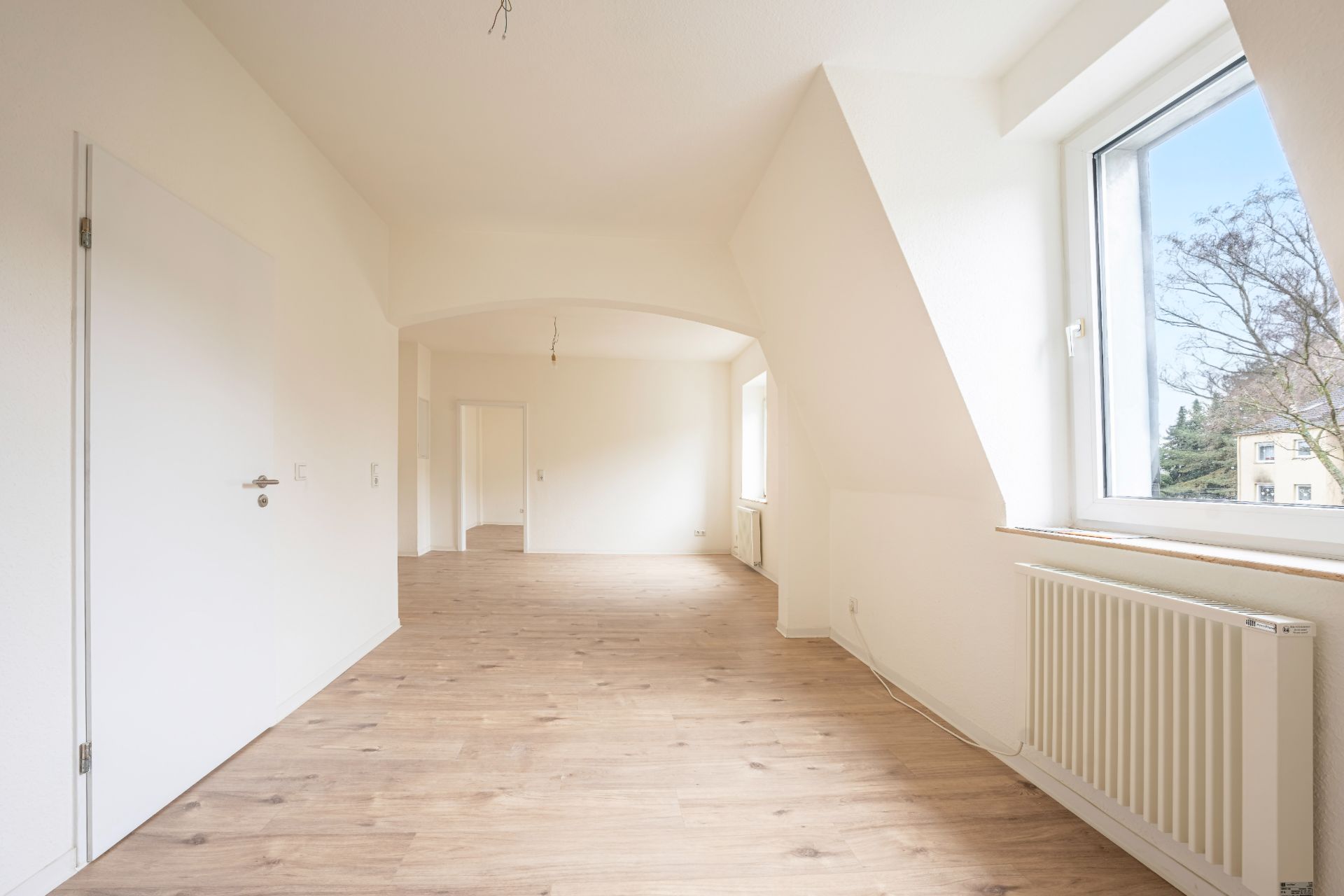 Heller Raum mit Holzfußboden, großen Fenstern und weißer Wand, Heizung unter dem Fenster.