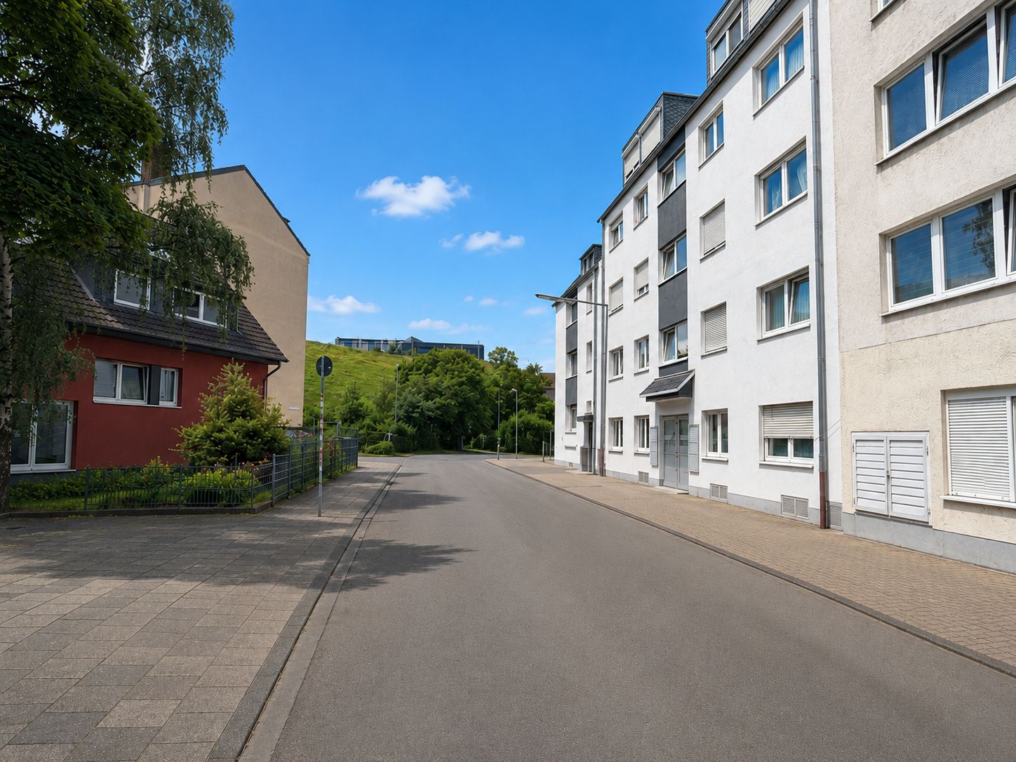 Ruhige Wohnstraße mit Mehrfamilienhaus und Einfamilienhaus bei sonnigem Wetter.