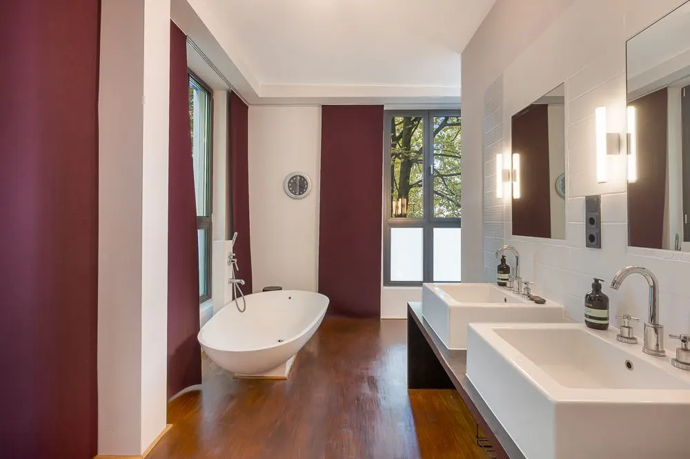 Modernes Badezimmer mit freistehender Badewanne, zwei Waschbecken und großen Fenstern.