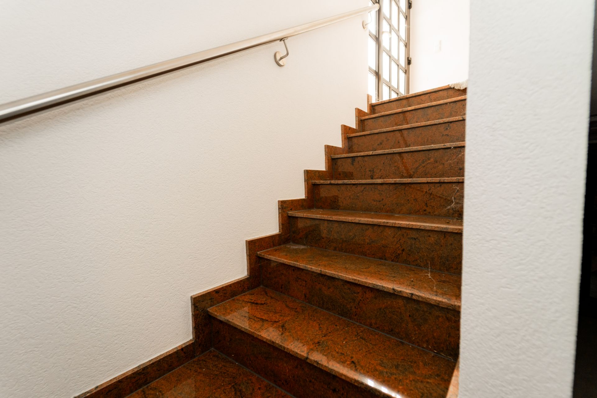Treppe mit braunen Stufen, weißer Wand und Metallhandlauf.
