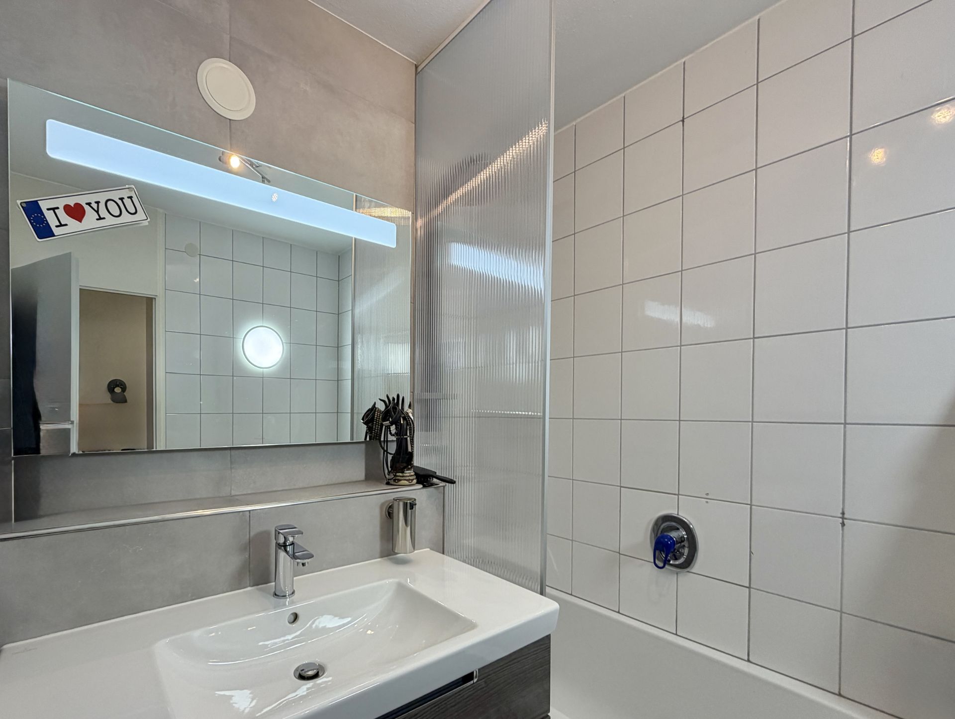 Modernes Badezimmer mit Waschbecken, Spiegel und weiß gefliester Badewanne.