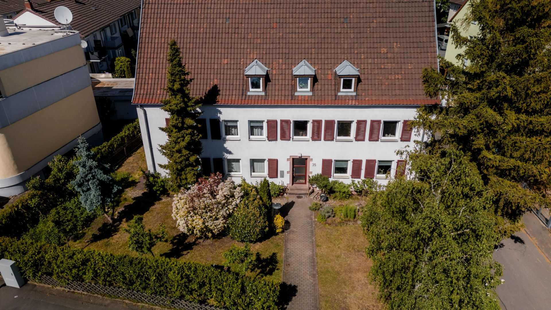 Zweistöckiges Wohnhaus mit Satteldach und gepflegtem Vorgarten, umgeben von Bäumen und Hecken.
