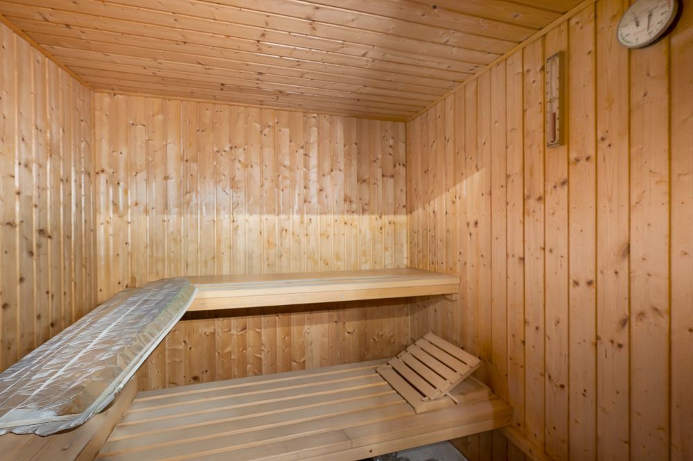 Innenansicht einer Holzsauna mit zwei Holzbänken und einer Wanduhr.