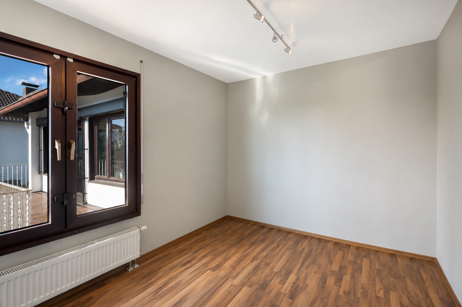 Leerer Raum mit Holzfußboden, großem Fenster und Heizkörper unter dem Fenster.