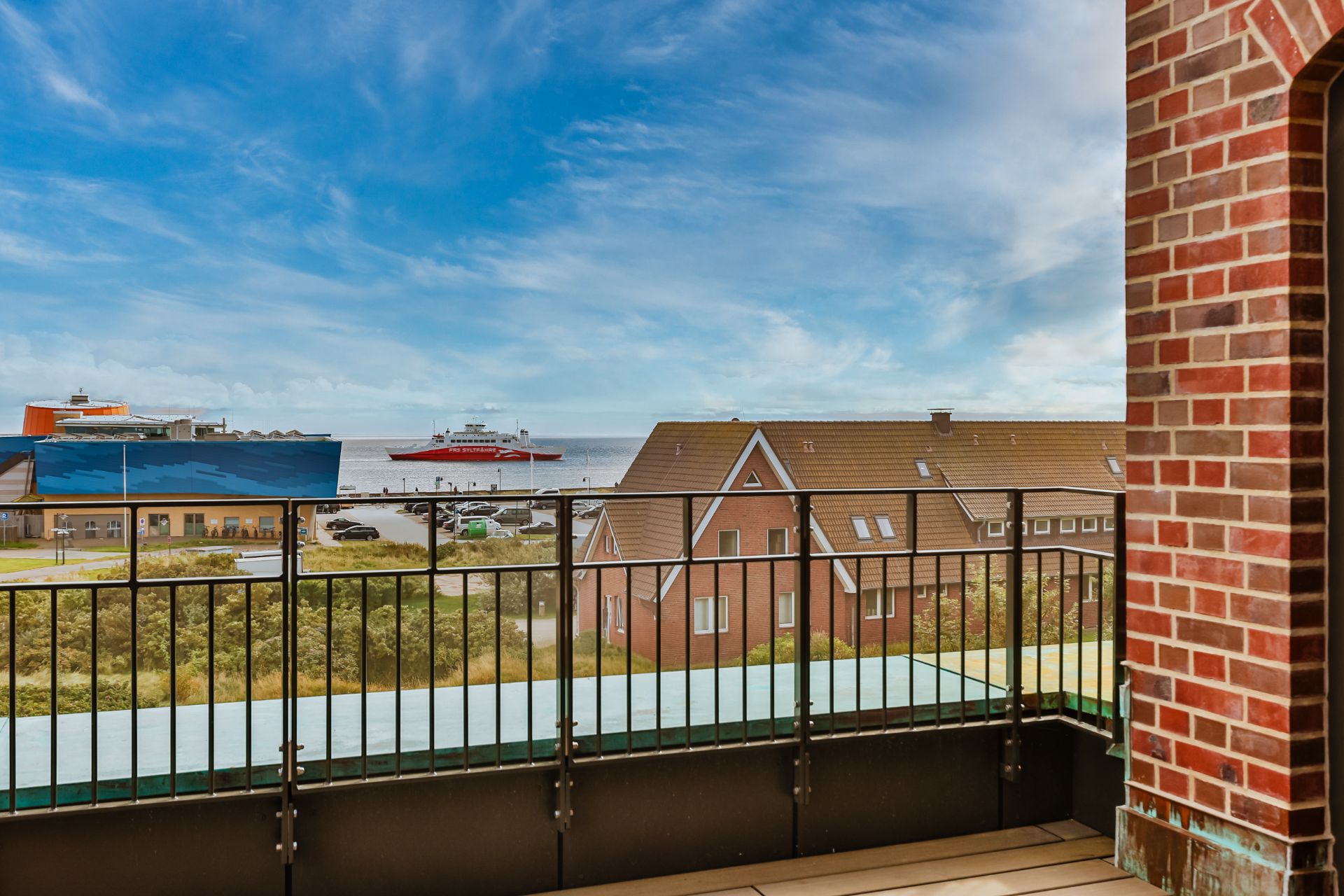 Balkon mit Metallgeländer, Blick auf Häuser, Wasser und Schiffe im Hintergrund.