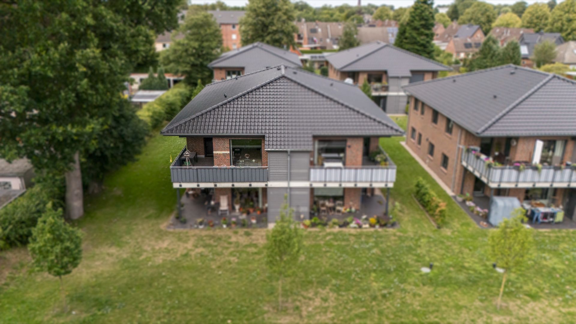 Mehrfamilienhaus mit Balkonen, umgeben von Rasen und Bäumen, aus der Vogelperspektive.