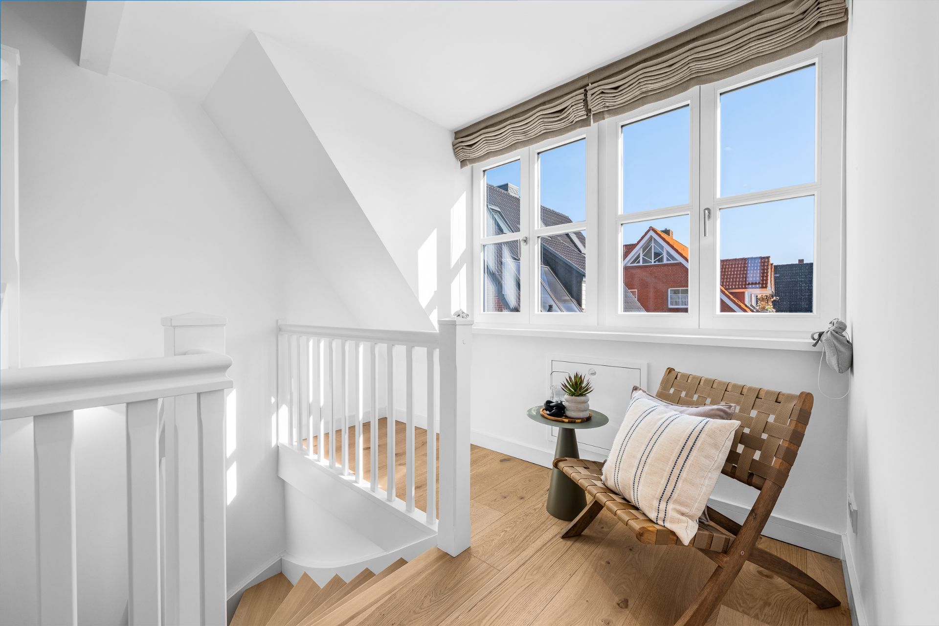 Helle Ecke mit Fenster, Stuhl mit Kissen, kleinem Tisch und Holztreppe.