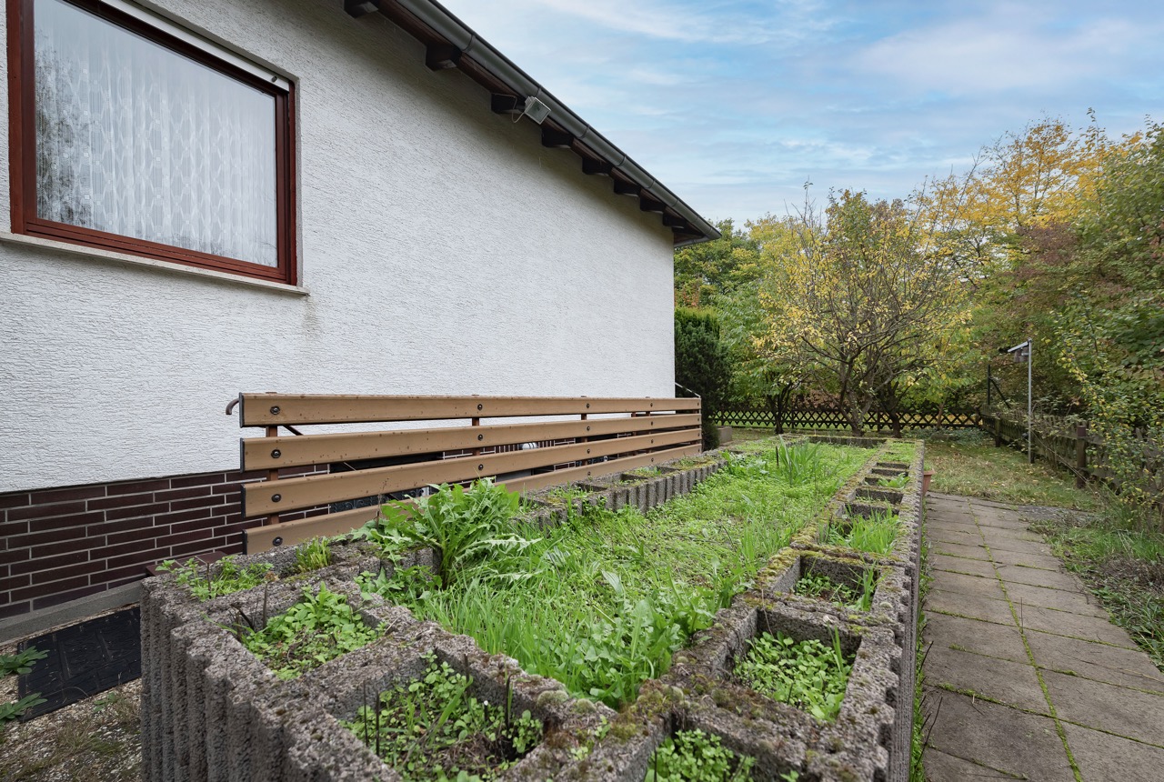Gartenbereich mit Steinbeeten und Gehweg neben einem Haus mit weißer Fassade.