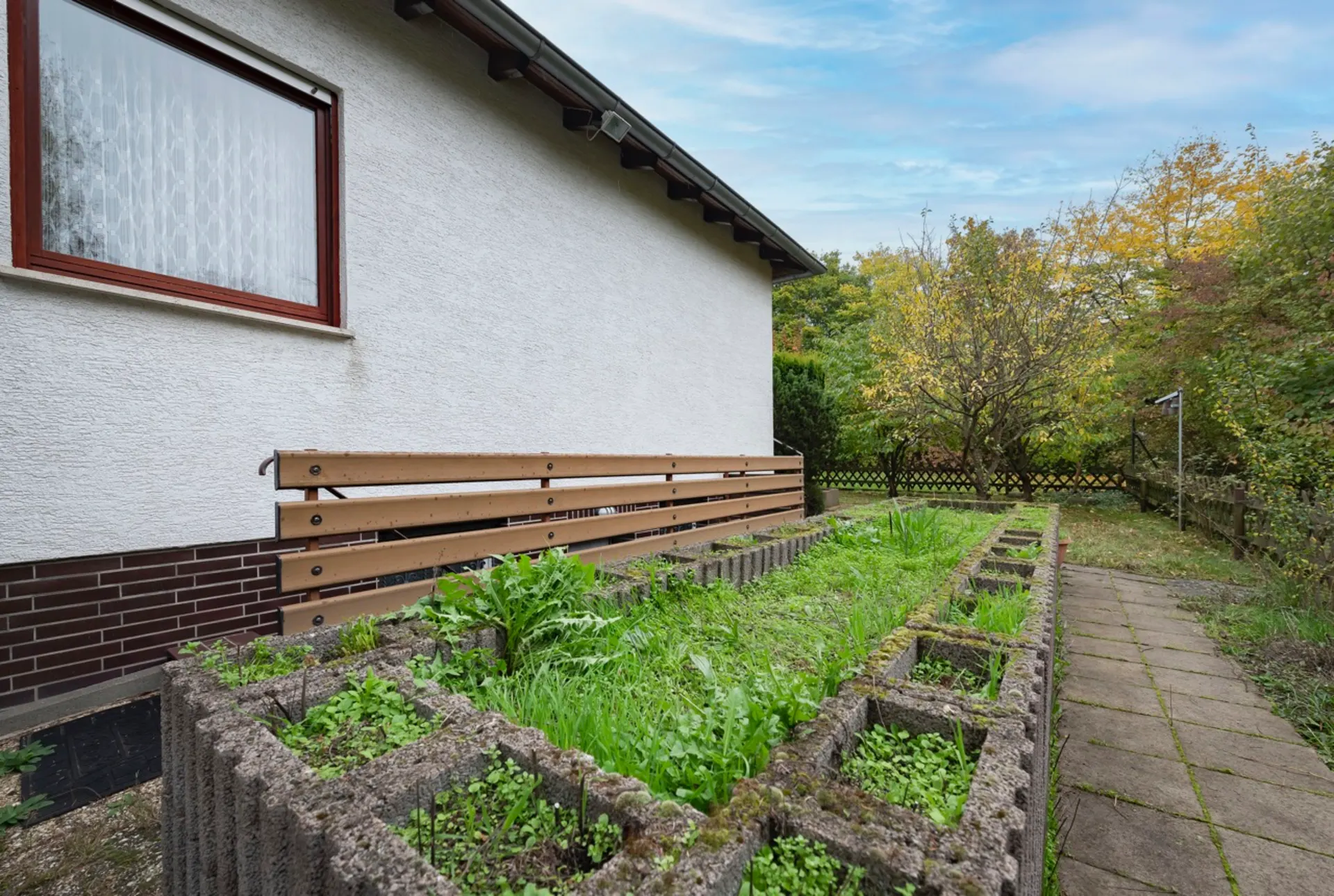 Gartenbereich mit Steinbeeten und Gehweg neben einem Haus mit weißer Fassade.