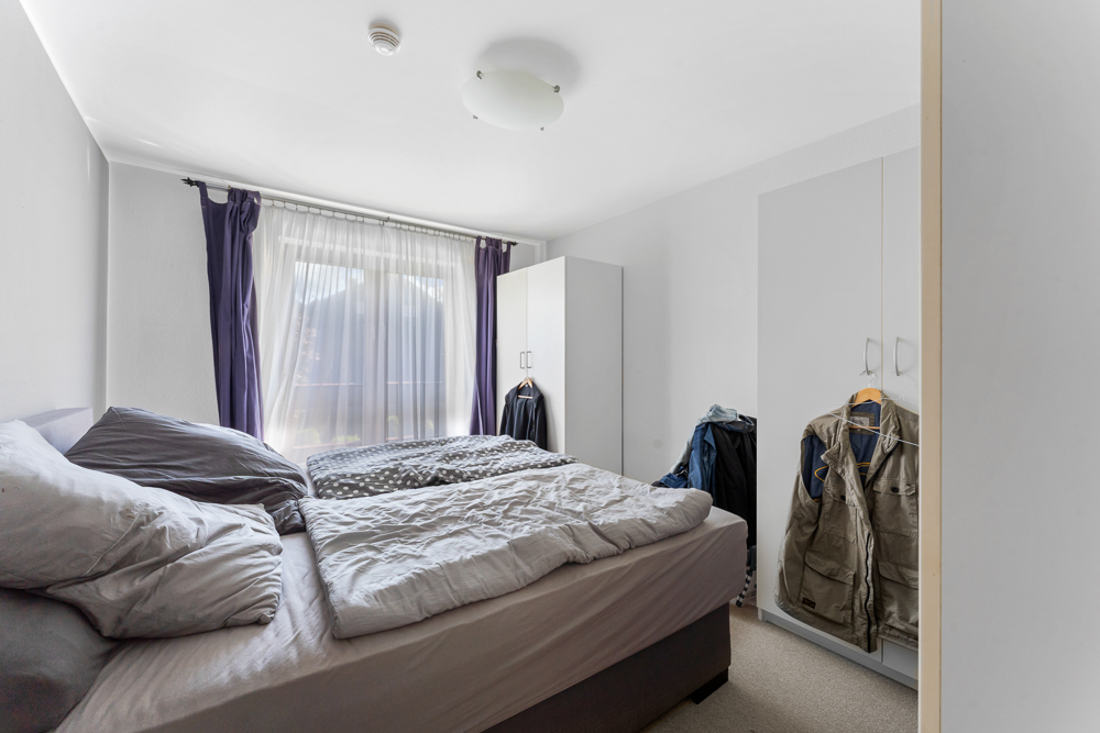 Helles Schlafzimmer mit Doppelbett, zwei Kleiderschränken und Fenstern mit Vorhängen.