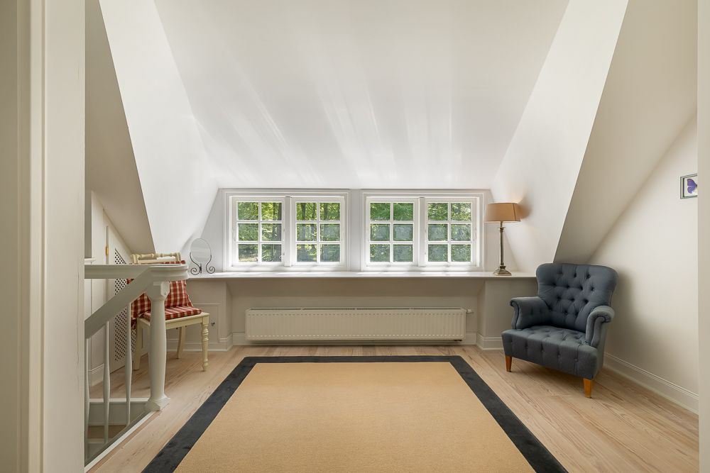 Heller Raum mit Dachschräge, vierfenstrigem Fenster, Sessel und Stehlampe auf hellem Holzboden.