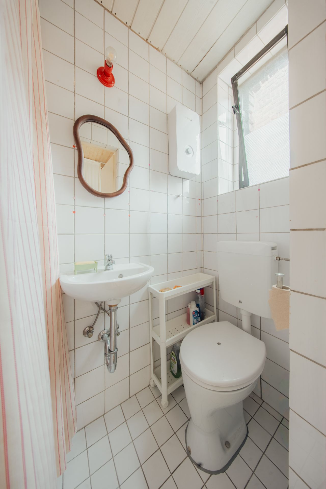 Kleines Badezimmer mit Toilette, Waschbecken, Spiegel und Fenster.
