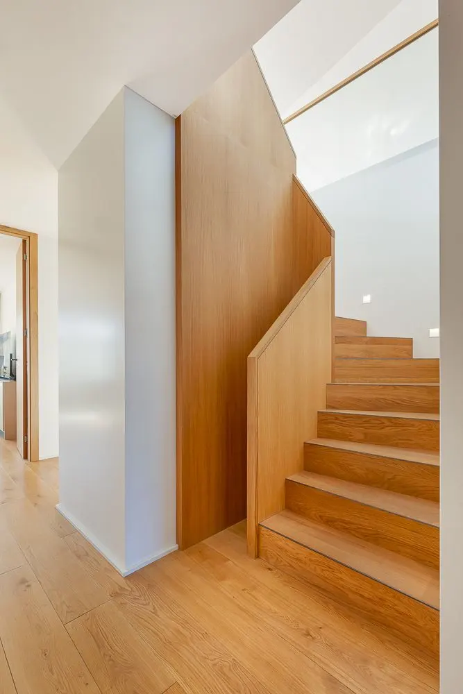 Helle Holztreppe mit Holzgeländer und Parkettboden in einem modernen Wohnhaus.