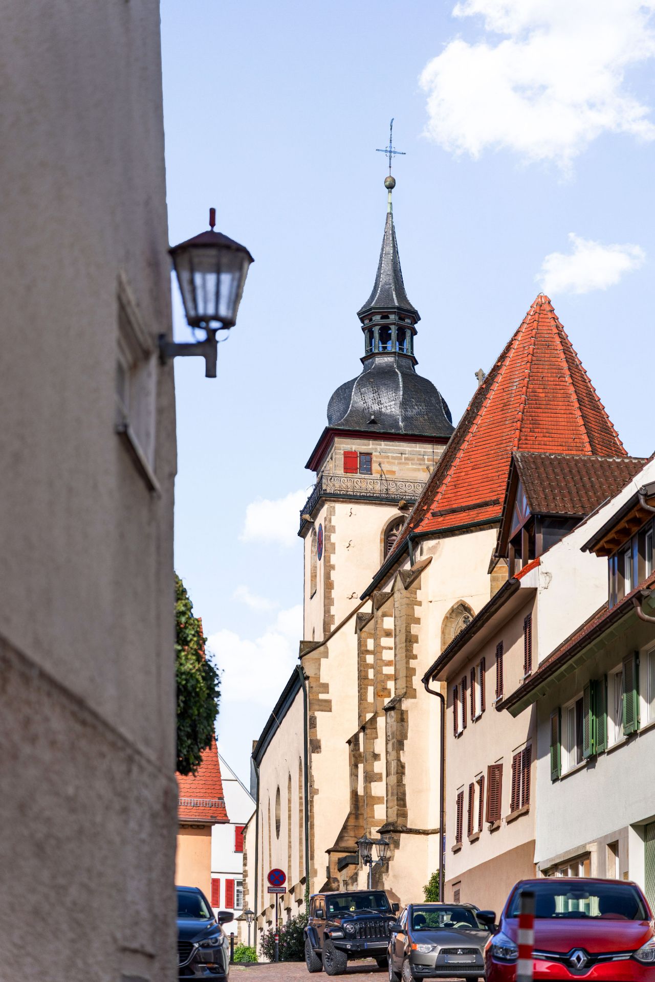 Schmale Straße mit parkenden Autos und einer Kirche im Hintergrund.
