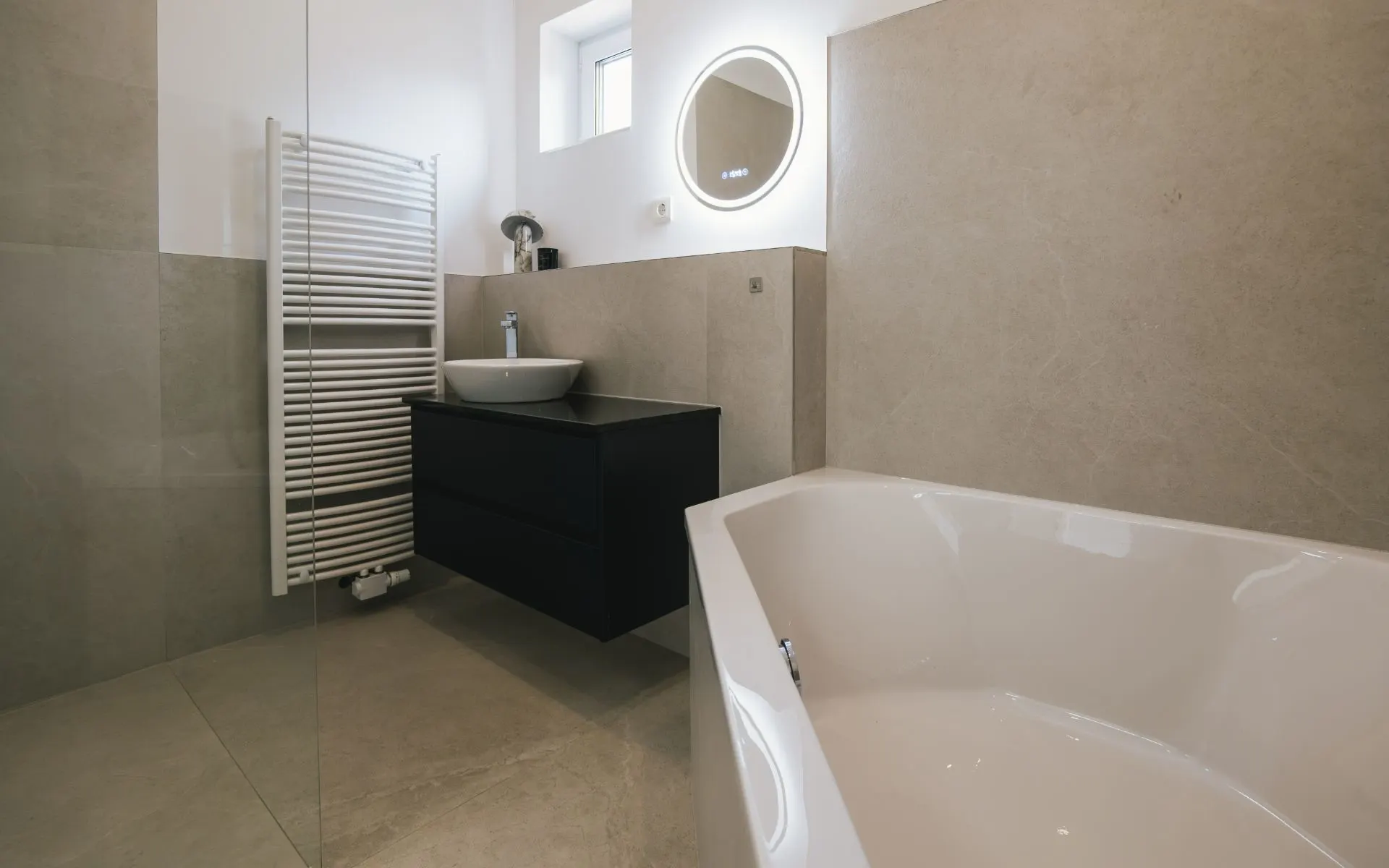 Modernes Badezimmer mit Badewanne, Waschbecken, Spiegel und Handtuchheizkörper.