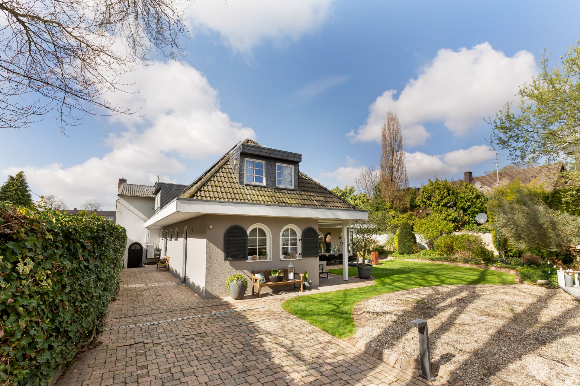 Modernes Einfamilienhaus mit Vorgarten, Terrasse und gepflasterter Einfahrt bei Tageslicht.