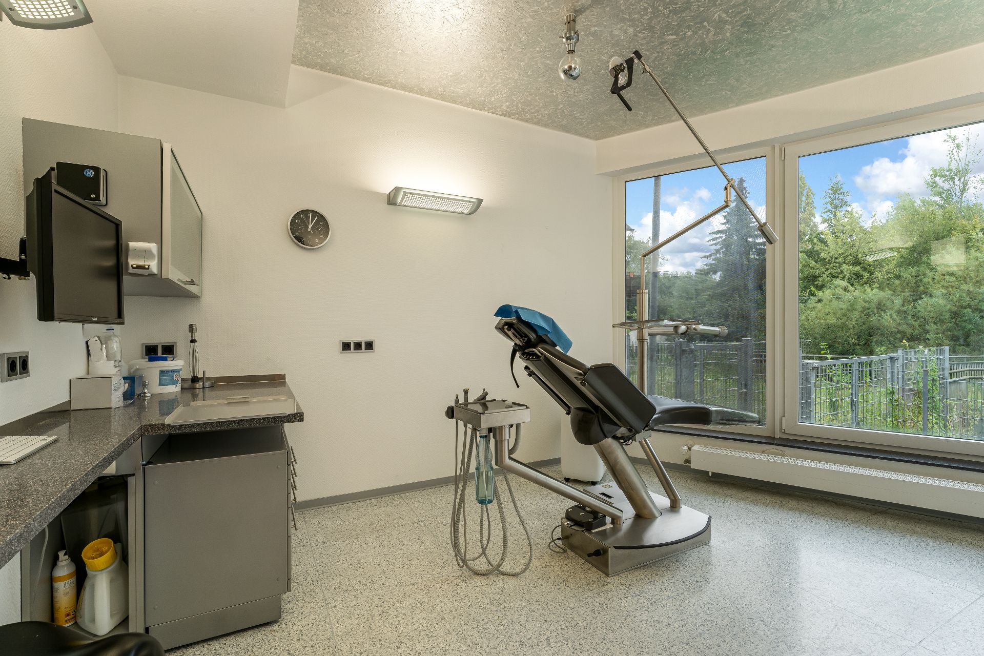 Behandlungsraum mit einem Zahnarztstuhl, großem Fenster und Arbeitsfläche mit Schränken.