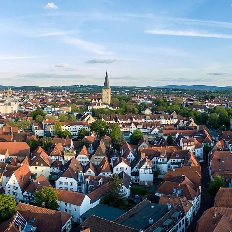 Schmale gepflasterte Straße mit Wohnhäusern und geöffneten Fenstern an beiden Seiten bei Tageslicht.