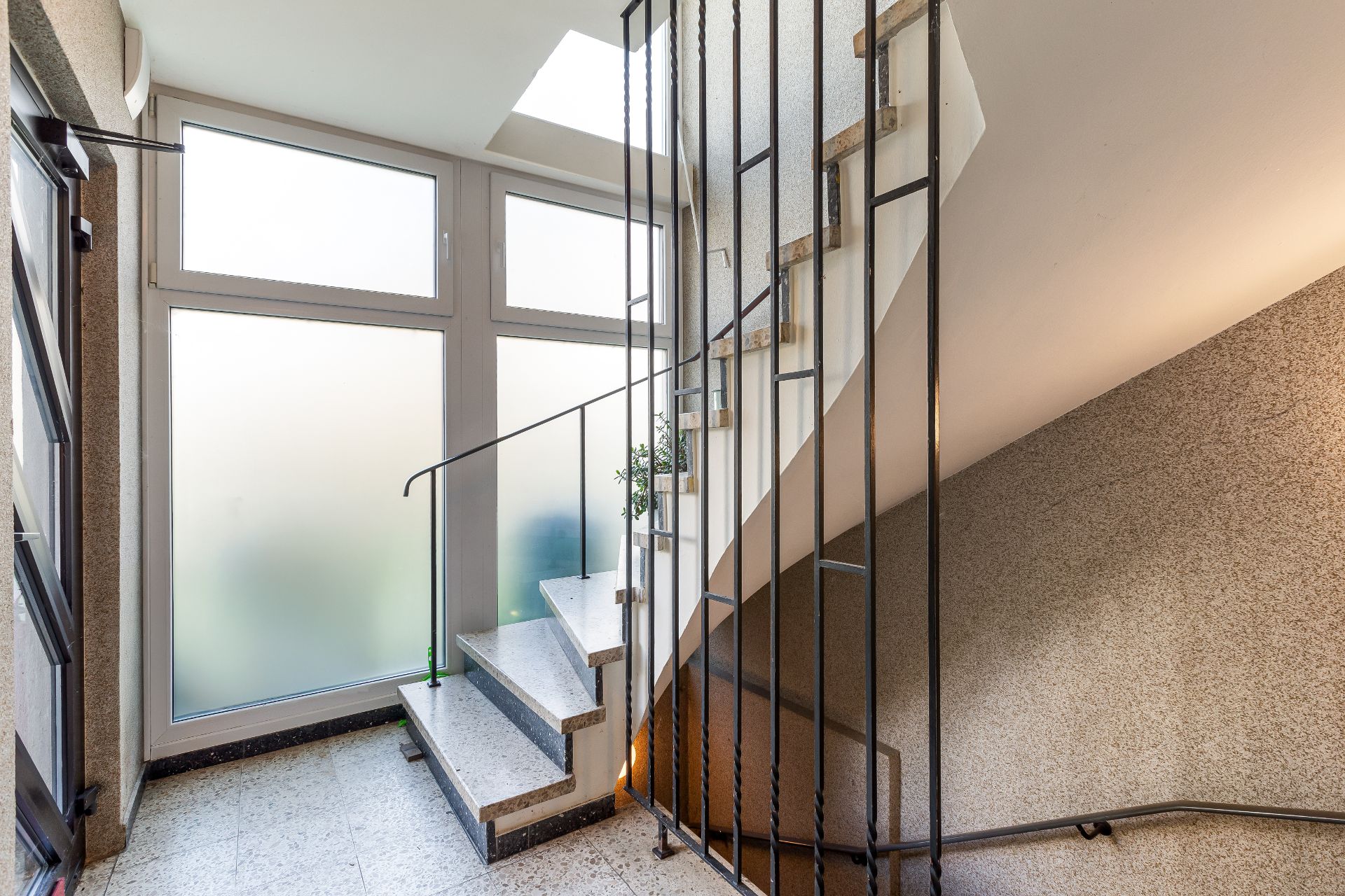Helle Treppe mit Metallgeländer und großen, milchigen Fenstern im Treppenhaus.