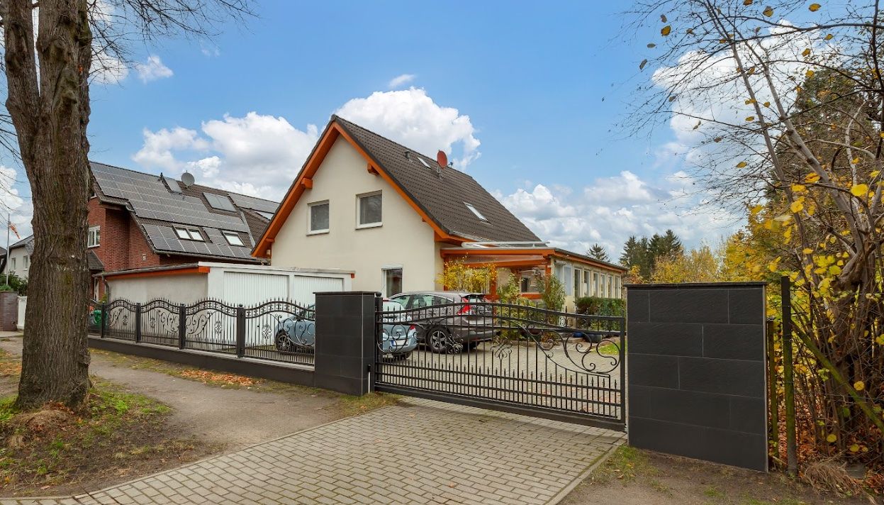 Einfamilienhaus mit Satteldach, Auffahrt, Metallzaun und mehreren geparkten Autos vor dem Haus.
