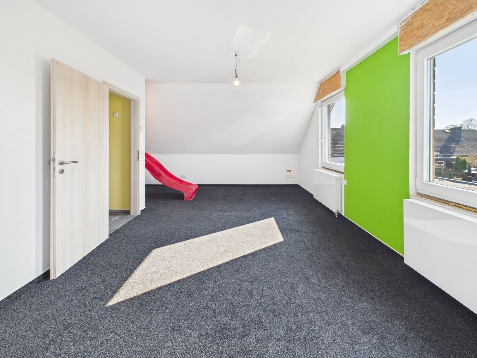 Heller Raum mit grün gestrichener Wand, Teppichboden und roter Rutsche.