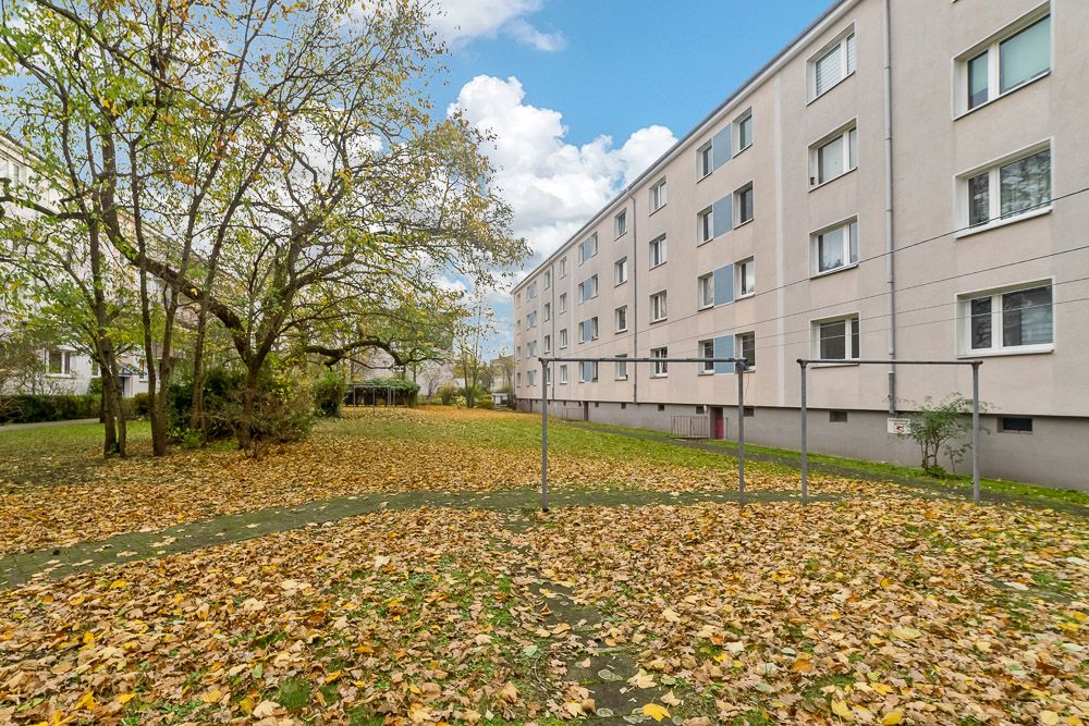 Hof mit Bäumen und Herbstlaub, daneben ein mehrstöckiges Wohngebäude.