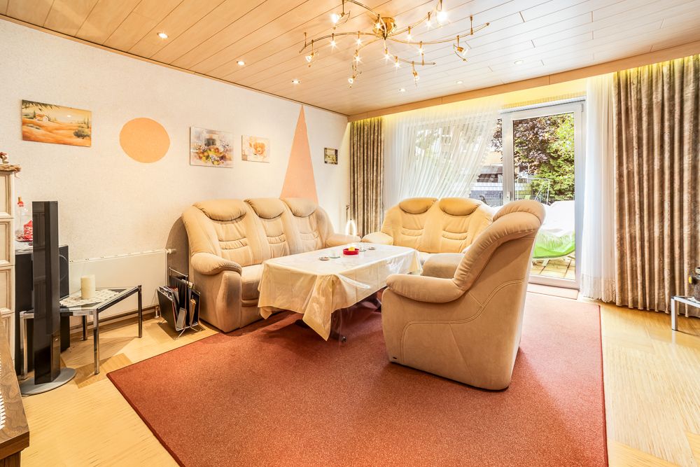 Helles Wohnzimmer mit drei beigen Sofas, Tisch, Teppich und Glas-Schiebetür zum Garten.