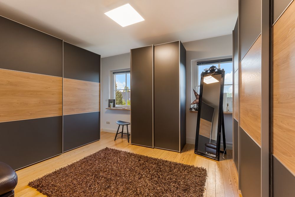 Modernes Schlafzimmer mit großen Schränken, Teppich, Spiegel und zwei Fenstern.