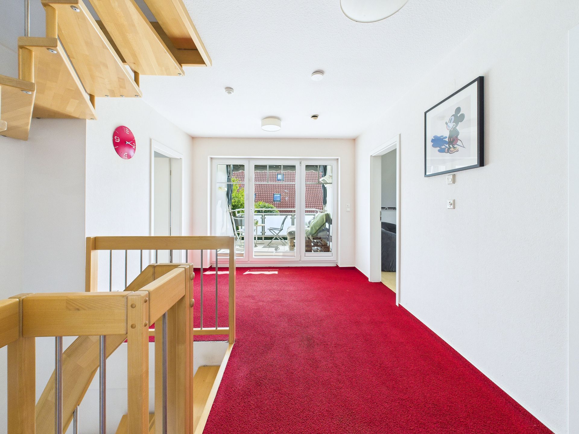 Heller Flur mit rotem Teppich, Holztreppe und Glastür zum Balkon.