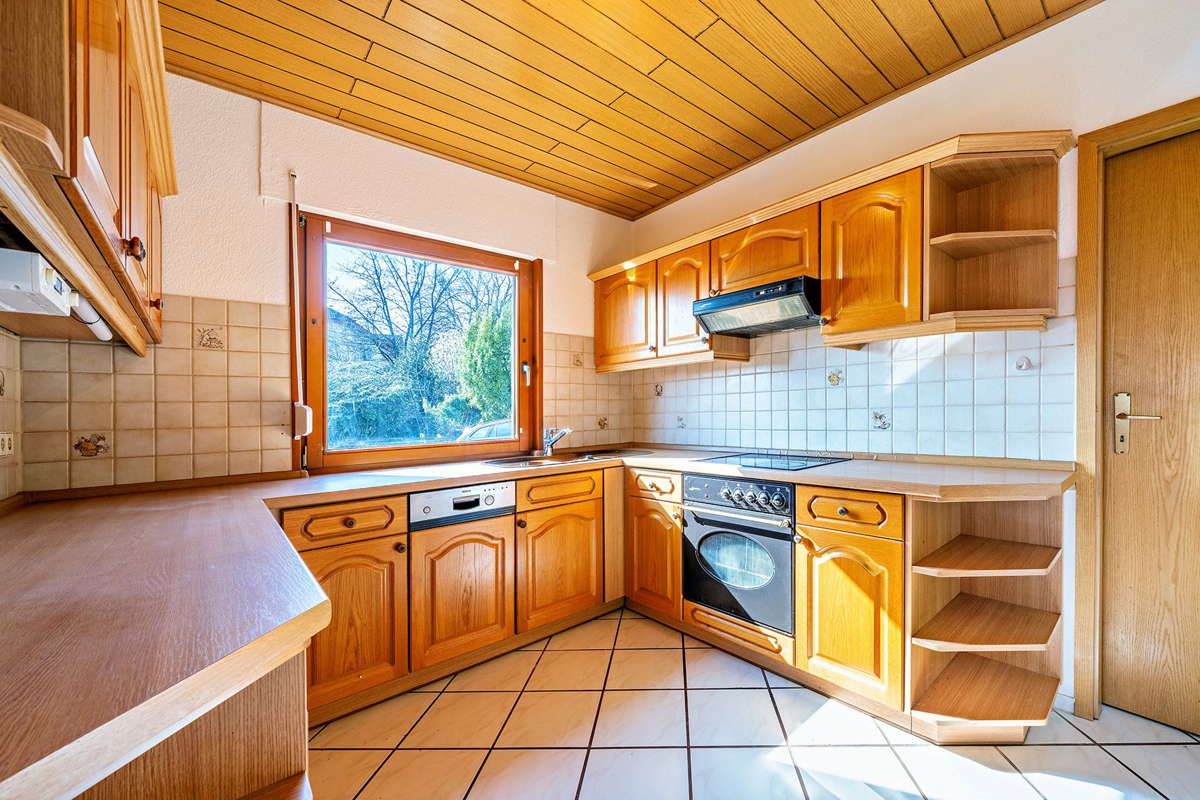 Helle Einbauküche mit Holzfronten, Eckfenster, Herd, Spülmaschine und Fliesenspiegel.