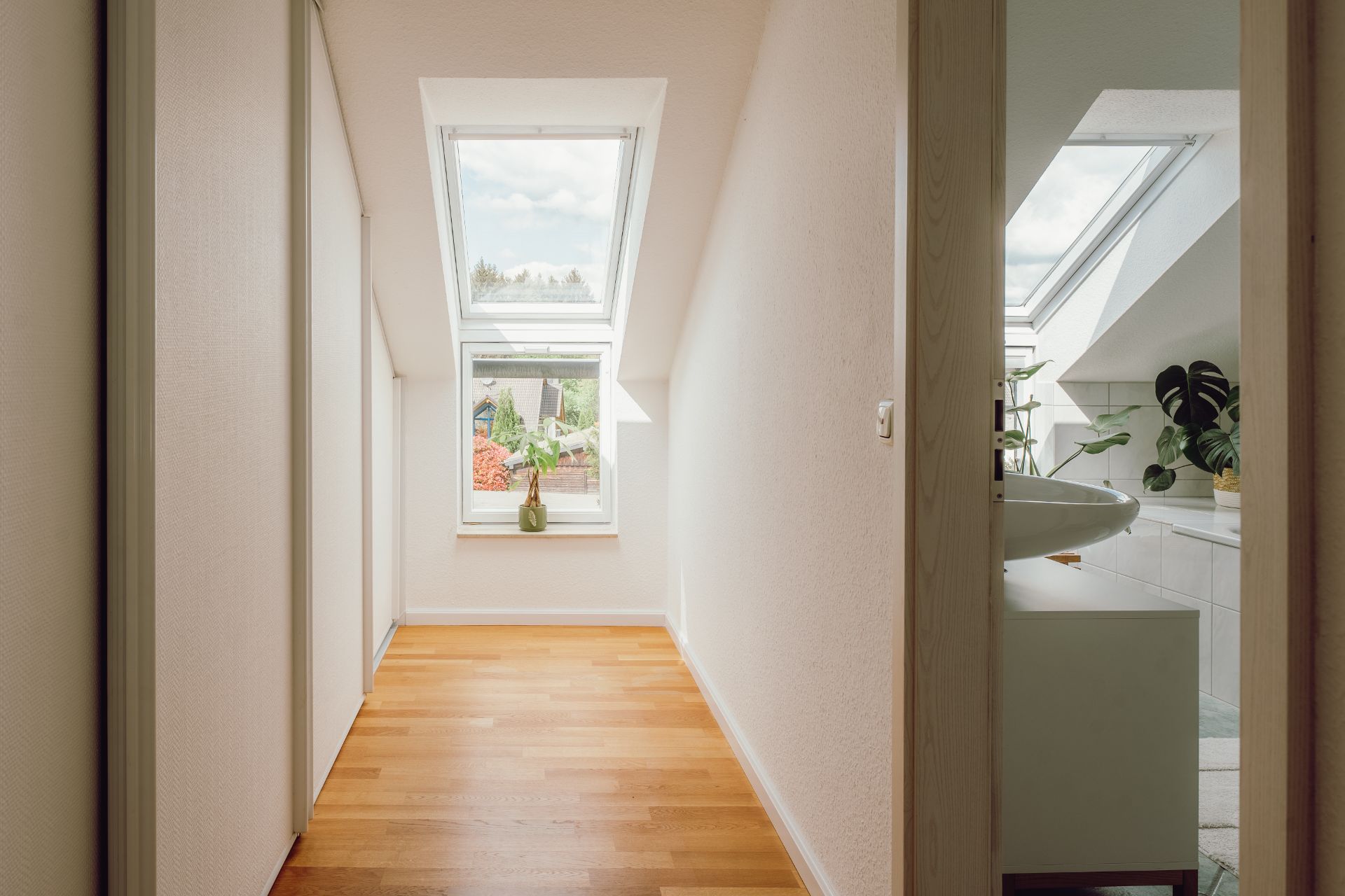 Heller Flur mit Dachfenster, Zimmerpflanze auf der Fensterbank und Blick ins Badezimmer.