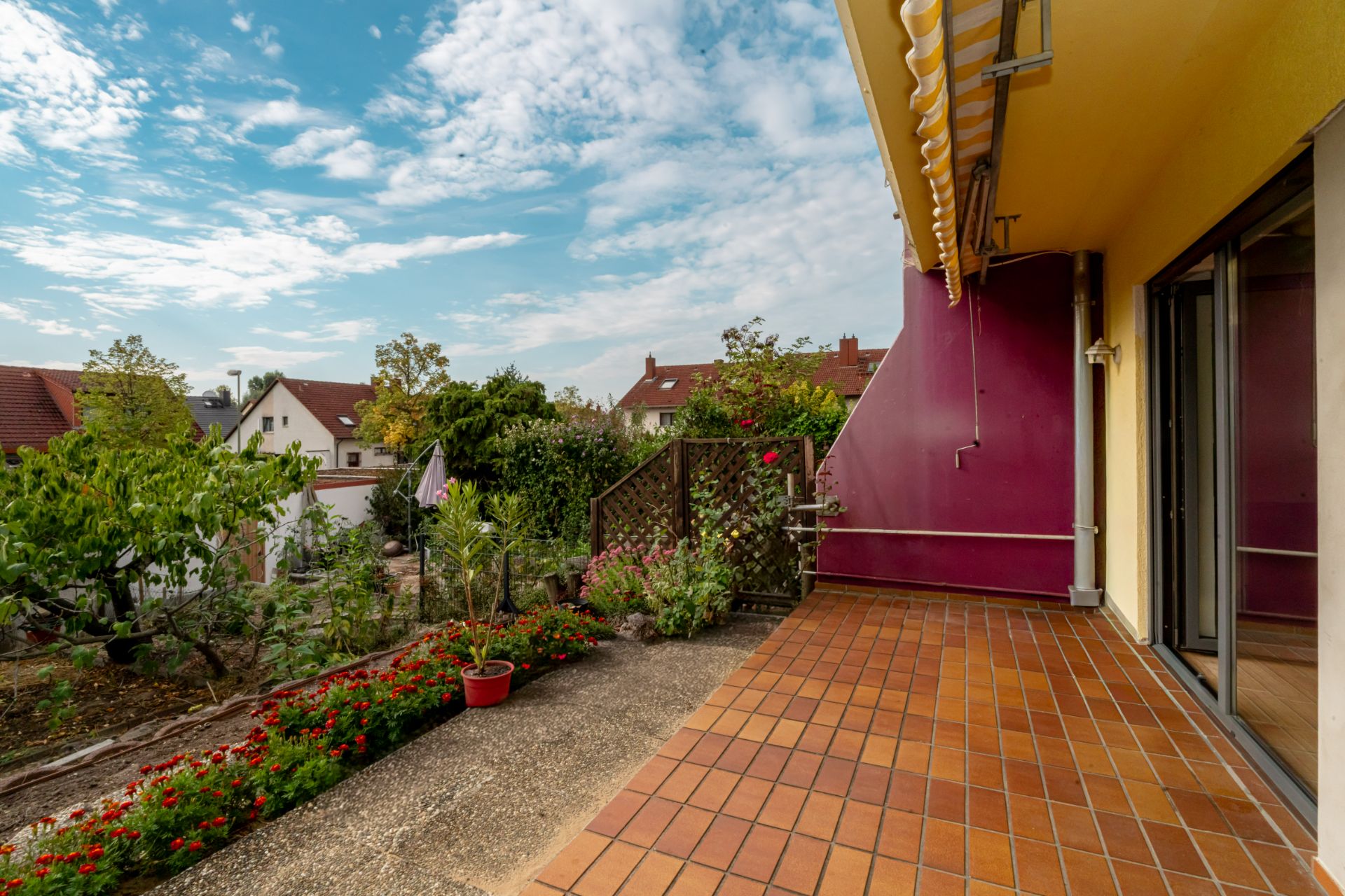 Terrasse mit Fliesenboden, Blumen und Blick auf Garten und Nachbarhäuser.