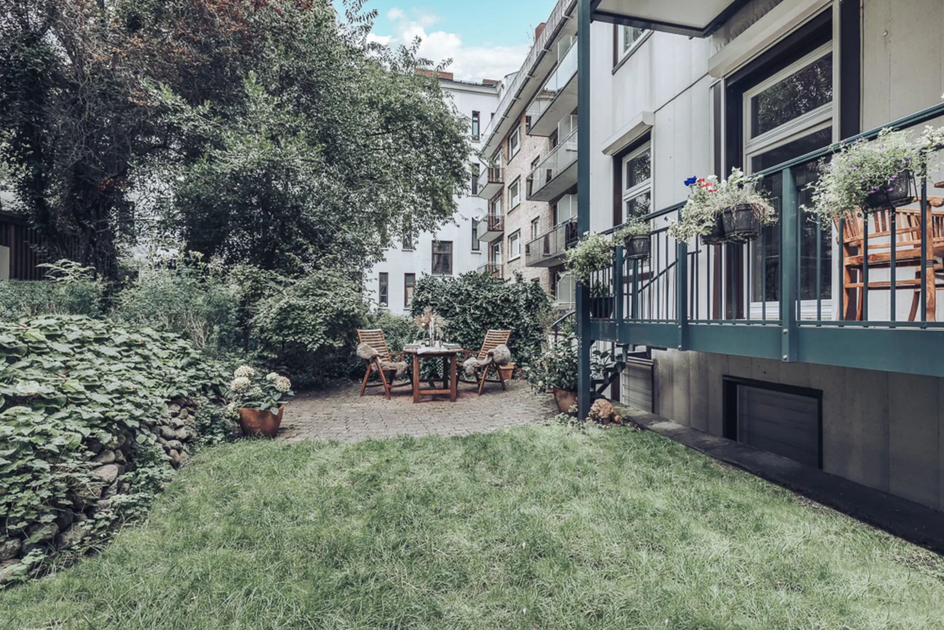 Garten mit Rasenfläche, Sitzgruppe und Balkon mit Blumenkästen an einem Wohnhaus.