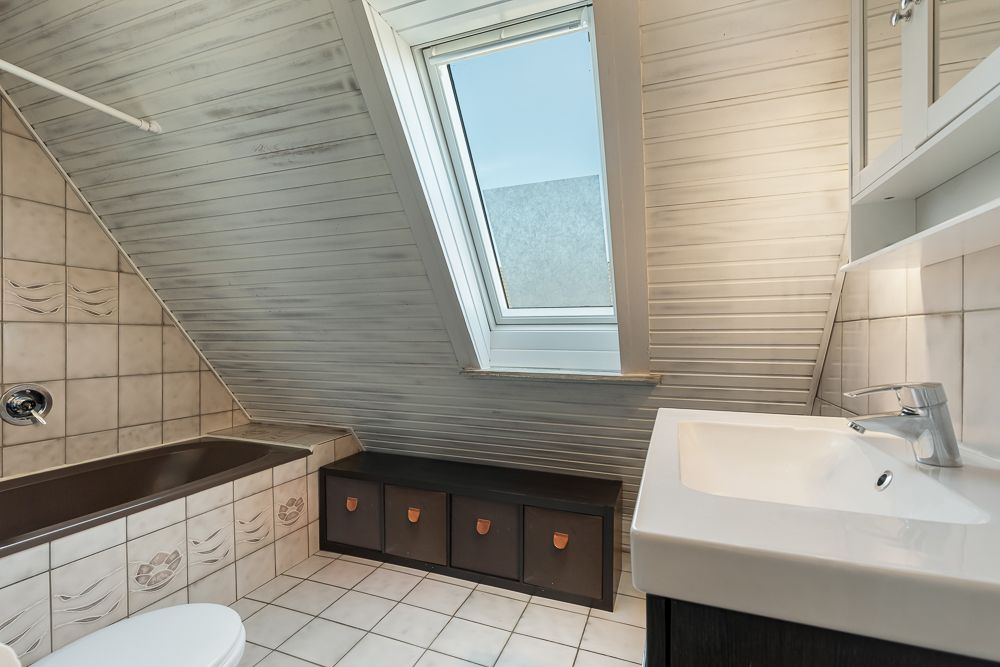 Badezimmer mit Dachschräge, Badewanne, Waschbecken, WC und Dachfenster.