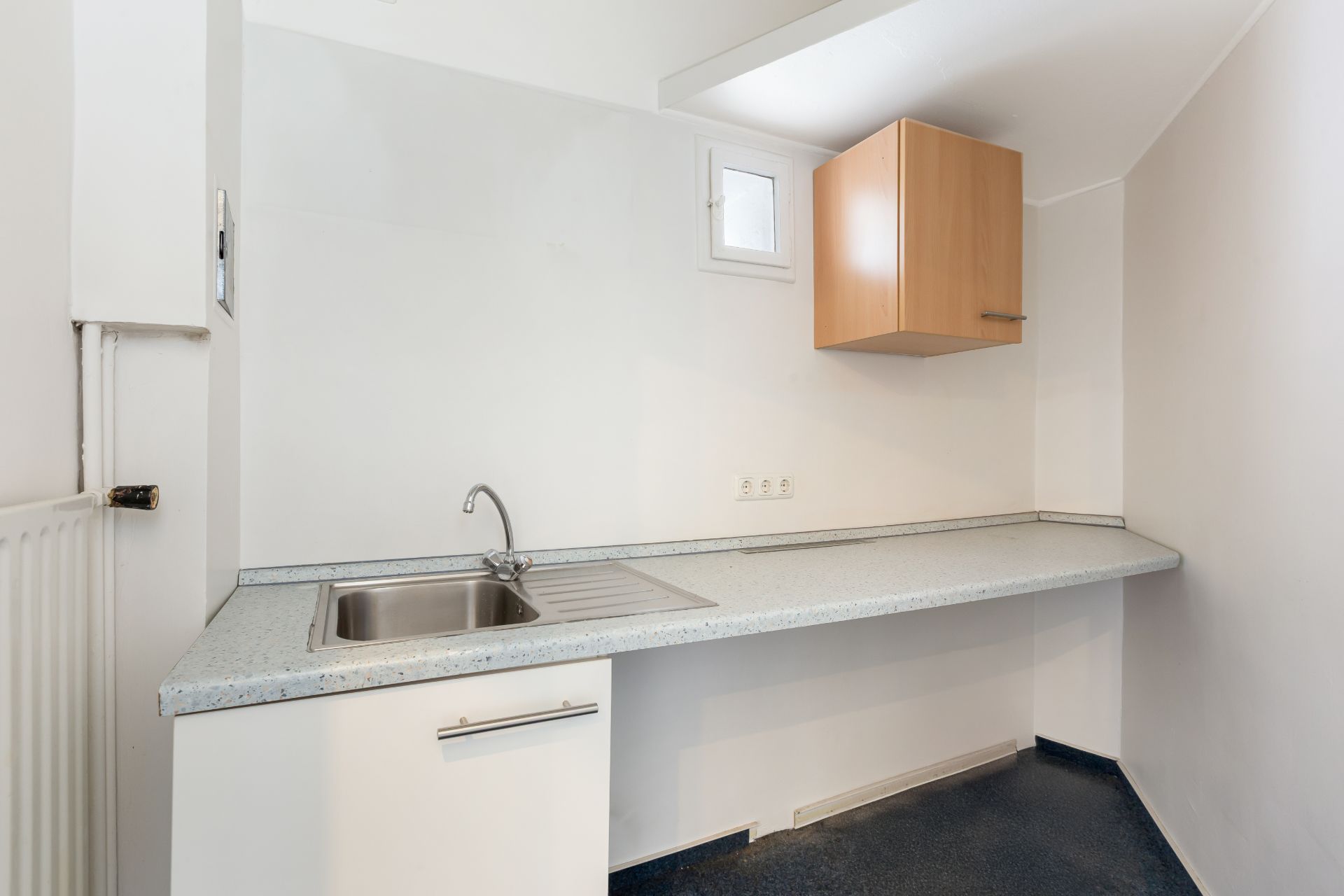 Kleine, helle Küchenzeile mit Spüle, Unterschrank und hängendem Holzschrank.
