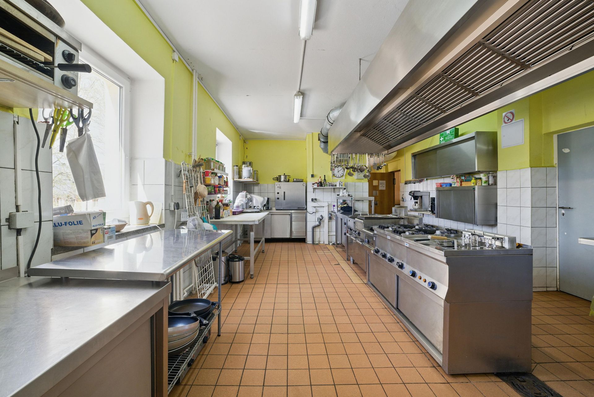 Große Küche mit Edelstahl-Arbeitsflächen, gasbetriebenen Herden und gelben Wänden.