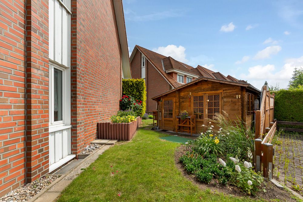 Garten mit Rasen, Blumenbeet und Holzhaus neben einem Backsteinhaus.