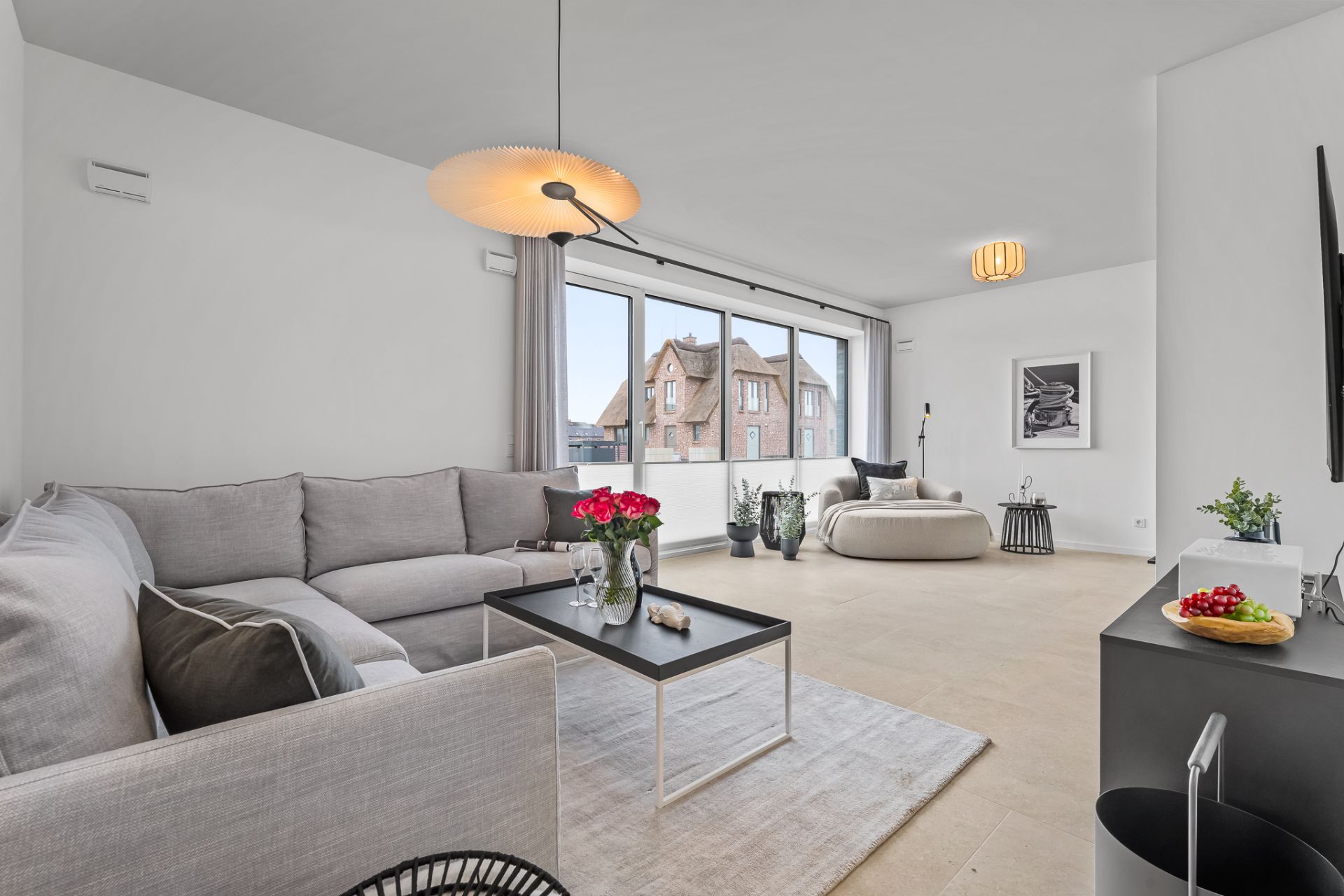 Helles Wohnzimmer mit grauem Sofa, Couchtisch, rundem Sessel und großen Fenstern.