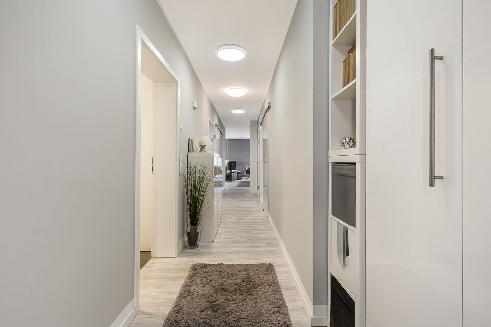 Heller Flur mit Teppich, Pflanzen und offenen Regalen in einer Wohnung.