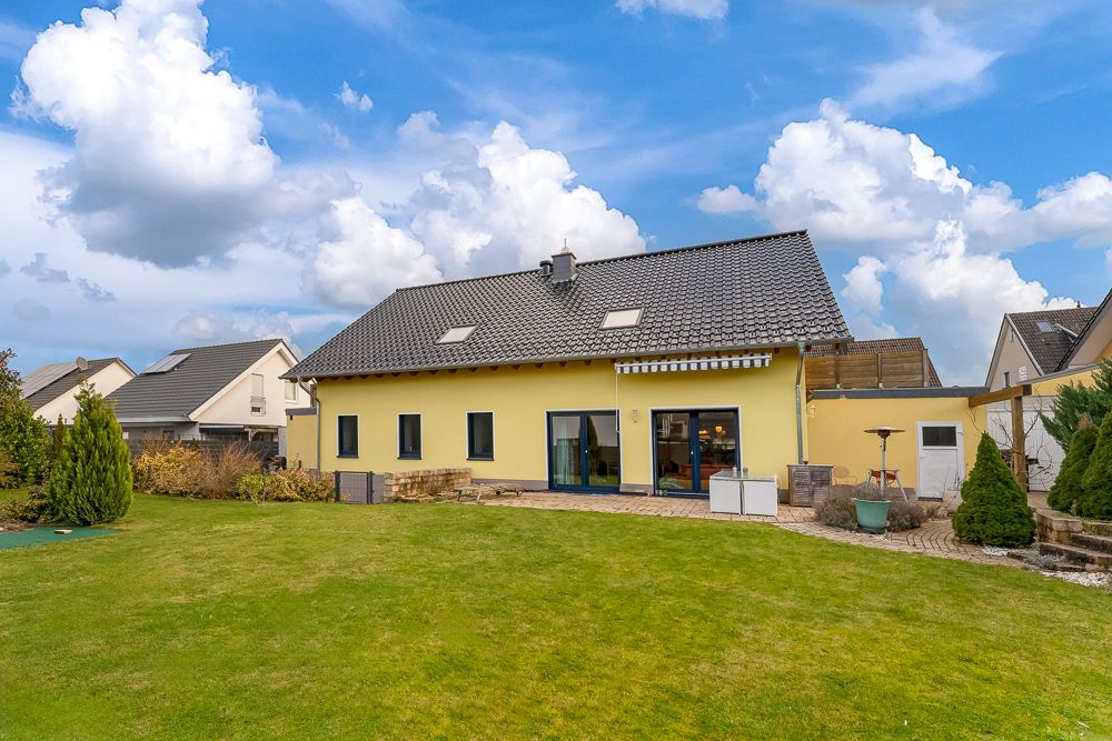 Gelbes Einfamilienhaus mit Garten, Terrasse und großen Fenstern, umgeben von anderen Häusern.