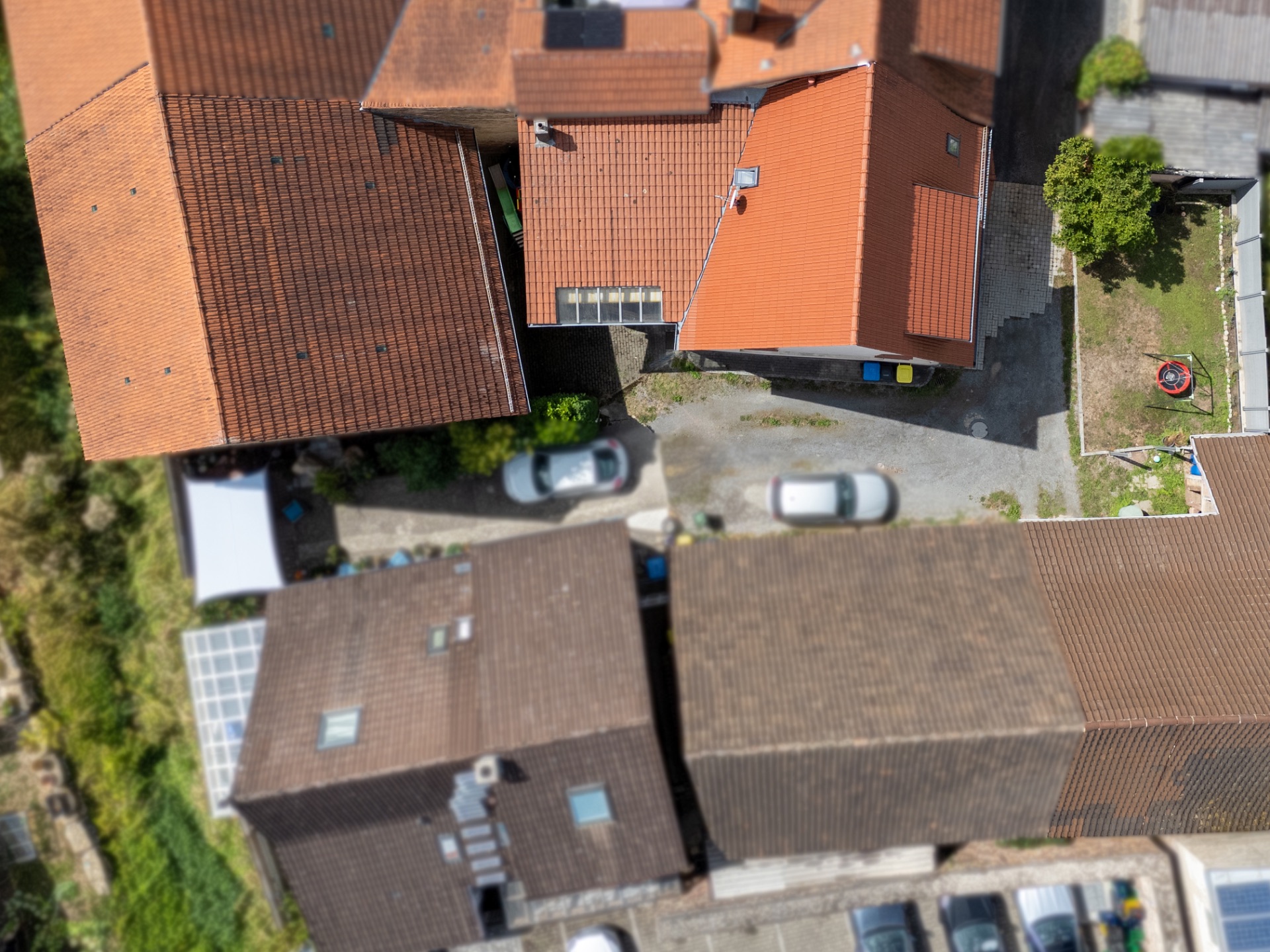 Luftaufnahme von mehreren Wohnhäusern mit roten und braunen Dächern, Autos und kleinem Hof.