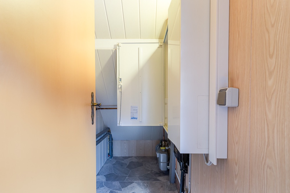Kleiner Hauswirtschaftsraum mit offenem Schrank, Rohren und Wandverkleidung aus Holz.