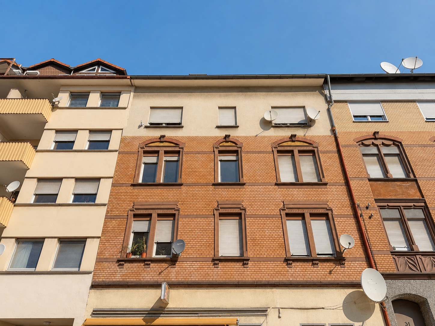 Fassade eines mehrstöckigen Wohnhauses mit mehreren Fenstern und Satellitenschüsseln.