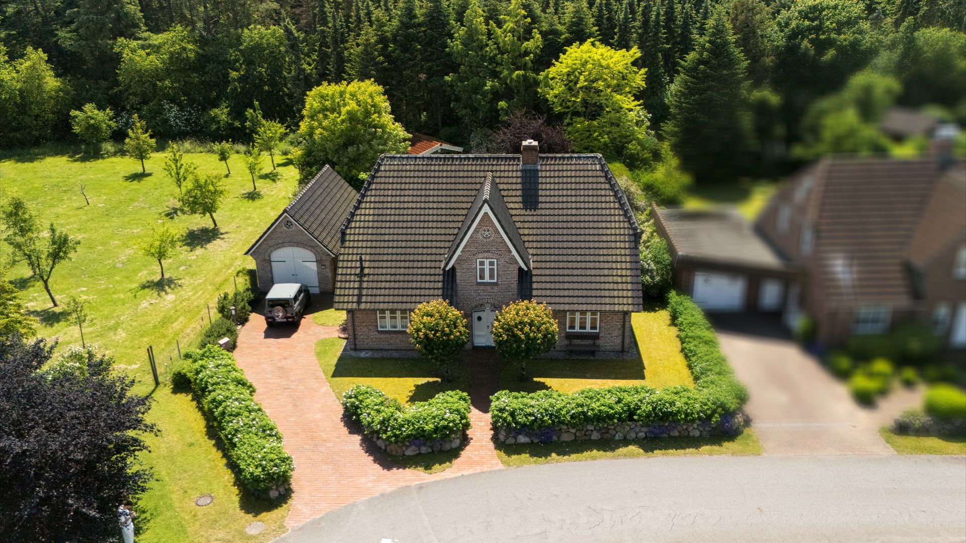 Luftaufnahme eines Einfamilienhauses mit Garage, Einfahrt und gepflegtem Garten.